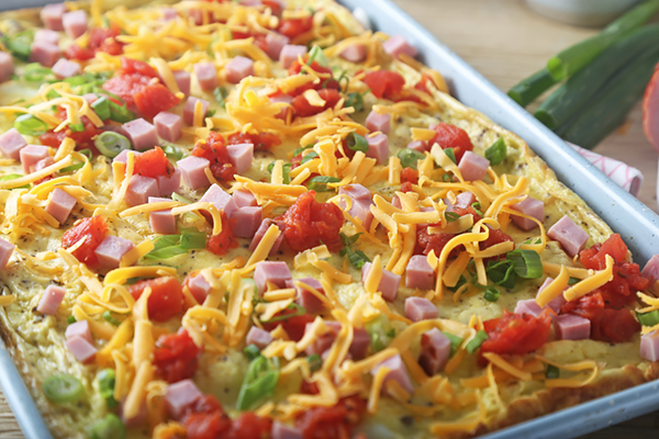 Diced ham, canned tomatoes, and shredded cheddar scattered over baked eggs on a sheet pan
