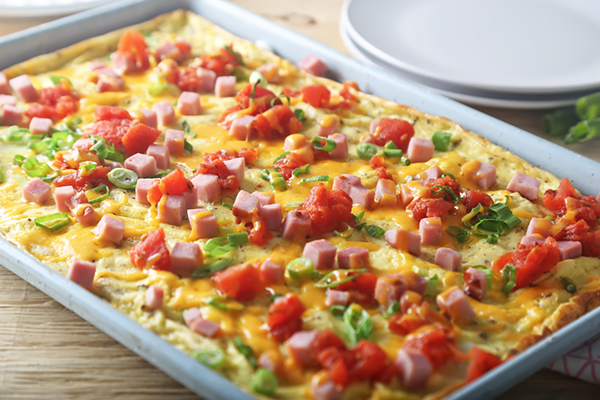 Melted cheddar cheese over ham and tomatoes on the sheet pan egg bake