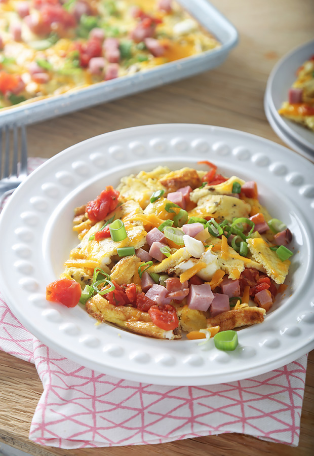 Western style egg scramble portioned on a white plate with ham, tomatoes, and green onion